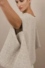 Poncho color beige con diseño a cuadros, cuello bote y terminaciones desflecadas. Tiene aberturas para los brazos en los laterales y detalles en cuero.