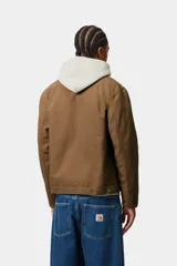Campera Carhartt WIP modelo Detroit Jacket, de color marrón con cuello corduroy negro y cierre frontal de cremallera. Presenta un bolsillo con cierre en el pecho con el parche del logo de la marca.