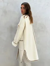 Sacón de punto color crudo con ribetes marrones, de corte largo y holgado, con cuello redondo, mangas largas y dos bolsillos frontales.