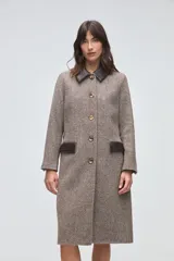 Tapado largo de lana fina con diseño de espiga en tonos beige. Presenta cuello camisero y solapas de bolsillos en cuero color suela, con cierre frontal de botones a tono.