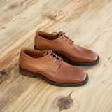 Zapato mocasín de cuero vacuno color negro, con cordones y punta redonda. Tiene taco de madera foliado en cuero de 2,5 cm y entre suela de goma de 1 cm.