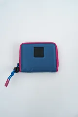 Billetera de diseño deportivo en color azul con bordes en fucsia. Presenta un parche frontal con el logo de la marca y un cierre con tirador de cordón ajustable.