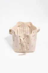 Bolso tipo saco color beige de piel vacuna, con estampado de palmeras pequeñas en marrón, cordón de ajuste frontal y asa regulable con hebilla metálica. Incluye el logo grabado de la marca en la parte inferior.