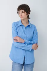 Camisa de estilo casual confeccionada en material tipo gamuza color marrón, con cuello clásico, cierre frontal con botones y costuras a la vista en tono contrastante.