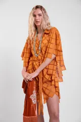 Vestido camisero oversize de color naranja en tela calada con diseño geométrico, cuello tipo solapa, mangas anchas y ruedo con terminación en picos. Cuenta con lazo ajustable en la cintura.