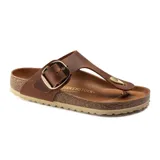 Sandalia tipo ojota Birkenstock modelo Gizeh, confeccionada en cuero nobuk aceitado color marrón coñac. Presenta una hebilla grande metálica dorada ajustable, plantilla anatómica de corcho y látex, y suela de goma antideslizante.