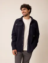 Sobrecamisa de polar azul marino con cierre frontal de botones a presión. Presenta bolsillos frontales con solapa, uno de ellos con cierre de cremallera adicional y detalles en contraste de material técnico.