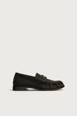 Mocasín de vestir para hombre confeccionado en piel con acabado en gamuza, color marrón. Presenta diseño tipo penny loafer con detalle de antifaz en el empeine, costuras visibles y suela contrastante con un ligero tacón.