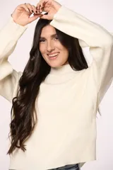 Buzo tejido de punto en color blanco crema, con cuello redondo alto y mangas largas con puños acanalados.