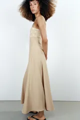 Vestido midi de color beige con escote recto adornado con un panel de encaje semitransparente, tirantes finos ajustables y falda fluida con cierre lateral con cremallera oculta.
