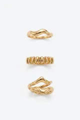 Set de tres anillos de metal dorado con diseños irregulares y orgánicos, incluyendo un modelo ondulado, uno con textura estriada y uno de diseño abierto entrelazado.