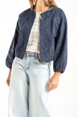 Campera tipo bomber color azul, con cierre frontal y diseño de bordado floral en toda la prenda. Presenta puños y ruedo con elástico, y un corte holgado.