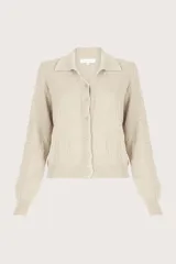 Sueter de punto color beige, con cuello polo, cierre frontal con botones y mangas largas con puños acanalados.