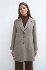 Saco corto entallado de lana fina, con cuello solapa, manga larga y cierre frontal con botones. Presenta un diseño clásico con textura de espiga en tonos tierra.