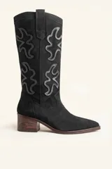 Bota de caña alta estilo tejano, confeccionada en gamuza negra con detalles de apliques decorativos en cuero al tono. Cuenta con taco cuadrado de madera y punta almendrada.