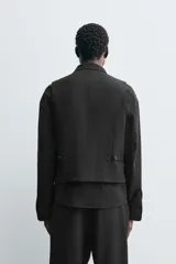 Chaleco de traje regular fit con cuello en pico y cierre frontal de botonadura. Presenta bolsillos de vivo en la parte delantera, detalle de bolsillo interior y cintura ajustable en los laterales con trabillas.