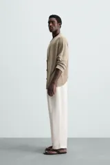 Pantalón blanco de corte relajado (relaxed fit) con pliegues frontales, bolsillos laterales y bolsillos traseros de vivo. Cierre frontal con cremallera y botón.