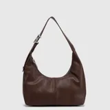 Cartera tipo hobo de Bubba, color marrón con textura granulada. Presenta un diseño minimalista con una correa ajustable que incluye una hebilla metálica decorativa con la letra B. Cuenta con cierre superior y logo de la marca grabado en la parte inferior.
