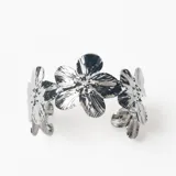 Brazalete rígido de metal plateado con diseño de flores unidas entre sí.