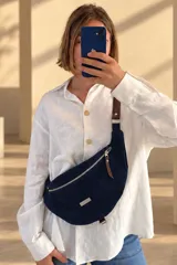 Riñonera urbana de gamuza azul marino, de diseño curvo con cierre frontal y detalles en cuero marrón y herrajes metálicos.
