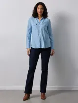 Camisa de manga larga en tela denim de color azul medio, con cuello clásico, botones frontales y dos bolsillos de parche con solapa en el pecho.