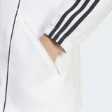 Campera deportiva Adidas de River Plate, color blanco, con detalles en rojo en los hombros y tres franjas negras en las mangas. Presenta cuello alto, cierre frontal y escudo del club bordado.