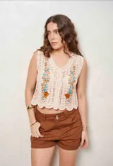 Chaleco de crochet color beige, sin mangas, con escote en V y botones frontales. Cuenta con bordados florales en tono marrón, celeste y ocre en la parte delantera y diseño con ondas en el ruedo.