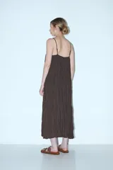 Vestido largo marrón oscuro, con tirantes finos y escote pronunciado que se ajusta con cordones en el centro. El tejido es arrugado o plisado.