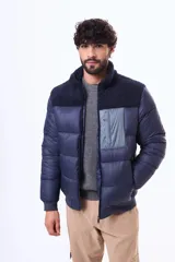 Campera puffer negra con paneles de textura tipo corderito en la parte superior del pecho y hombros. Cuenta con cierre frontal, puños y ruedo acanalados, y un bolsillo vertical con cierre en el pecho.
