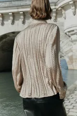 Camisa de manga larga con cuello solapa, confeccionada en tejido satinado con textura efecto arrugado y cierre frontal con botones dorados.