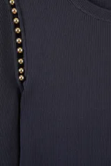 Sweater de punto fino color negro, con cuello redondo y mangas largas. Presenta un diseño ajustado con un corte asimétrico en el ruedo delantero y detalles de cuentas doradas en las costuras de los hombros.