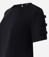 Blusa negra de crepé con cuello redondo y mangas cortas decoradas con lazos aplicados.