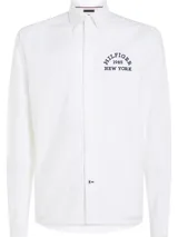 Camisa blanca de corte regular y manga larga, con logo bordado en el pecho y botón a contraste.