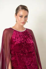 Vestido largo de fiesta color granate, confeccionado en terciopelo con cuello redondo adornado con strass y capa de chifón que nace de los hombros.