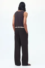 Pantalón sastrero de sarga en color marrón oscuro, con corte holgado, piernas amplias con raya marcada, cierre frontal con botón y corchete ocultos, bolsillos laterales al bies y bolsillos traseros insertados.