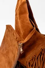 Bolso tipo hobo de gamuza color marrón, con diseño de flecos en los laterales y correa integrada al cuerpo del bolso.