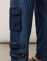 Jean de corte cargo y estilo holgado, con diseño de rayas verticales en tonos de azul. Presenta bolsillos laterales con solapa y detalles de tiras ajustables con hebillas en los tobillos.