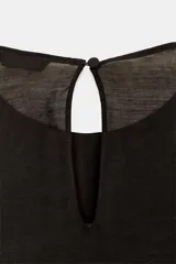 Blusa de cuello redondo y manga larga, color marrón oscuro. Presenta volantes en el frente y en los puños, y un bajo asimétrico. Cierre en la espalda con abertura y botón forrado.