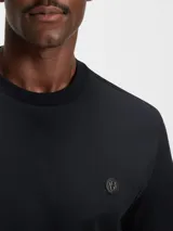 Remera de corte regular, color negro, con cuello redondo y detalle de monograma metálico en el pecho.