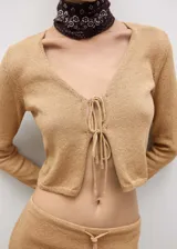Cardigan de punto color tostado, con cuello en pico, diseño corto y cierre frontal mediante lazos. Posee mangas largas y un tejido de textura ligera.