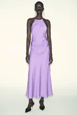 Vestido midi de satén color lila, con cuello halter y tirantes finos. Presenta un detalle de nudo en la cintura y espalda descubierta.