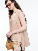 Camisa sin mangas color beige claro con efecto teñido en frío y aspecto gastado. Presenta cuello clásico, cartera oculta y ruedo irregular, más largo en los laterales.