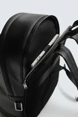 Mochila de diseño minimalista en color negro con acabado grabado. Cuenta con un compartimento principal con cierre de cremallera, un bolsillo frontal con cierre y un compartimento posterior acolchado para dispositivos electrónicos. Incluye asa de mano superior y dos asas de hombro ajustables.