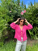 Blusa fucsia de lino con escote en V y mangas largas abullonadas con puños elásticos. Se cierra con lazos en la parte delantera.