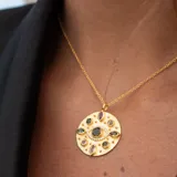 Collar dorado con colgante circular con diseño de ojo y piedras turmalinas multicolor y topacio blanco.