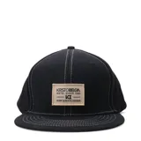 Gorra tipo snapback color negro con costuras blancas visibles y parche rectangular beige con logo de la marca en el frente.