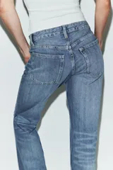 Jeans de tiro bajo y cinco bolsillos, con diseño de pierna ancha y larga. Presenta roturas y desgastes sutiles en la parte delantera. Cierre frontal con cremallera y botón metálico.