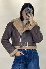 Campera tipo aviador de cuero sintético marrón con interior y detalles de corderito beige. Presenta cierre frontal cruzado, cuello solapa amplio, puños con corderito y cinturón ajustable en la cintura con hebilla metálica.