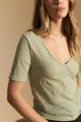 Top de manga corta confeccionado en tejido jacquard con textura en relieve. Presenta escote en V y un diseño frontal con líneas diagonales que crean un efecto cruzado.