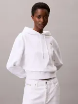 Buzo con capucha Calvin Klein de corte cropped, confeccionado en tejido de algodón y poliéster. Presenta un diseño minimalista en color blanco con el logotipo de la marca bordado en pequeño en el pecho y cordones ajustables en la capucha.